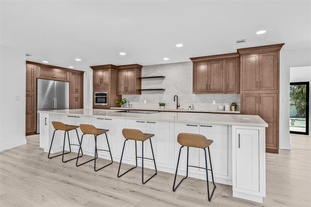 A modern kitchen features a large white island with bar stools, wood cabinetry, and stainless appliances — 4495 CLEARWATER HARBOR DRIVE S, LARGO, FL