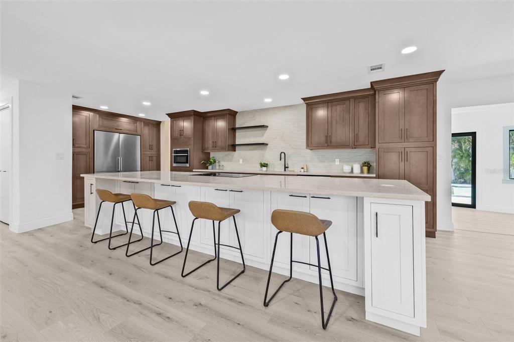 A modern kitchen features a large white island with bar stools and brown wood cabinetry — 4495 CLEARWATER HARBOR DRIVE S, LARGO, FL