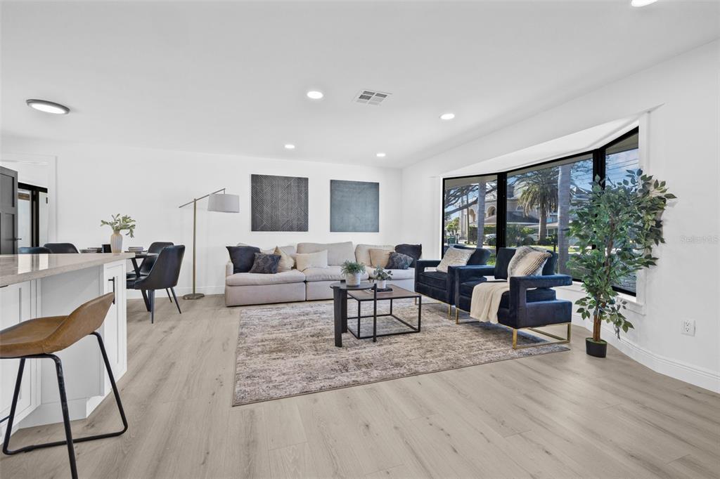 A bright living room features light wood flooring, a large sectional sofa, and bay windows — 4495 CLEARWATER HARBOR DRIVE S, LARGO, FL