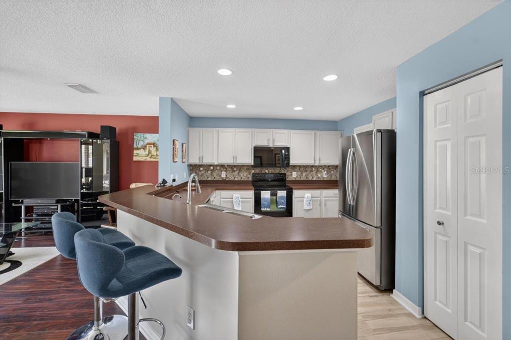 A kitchen features white cabinets, a brown countertop, stainless steel appliances, and blue bar stools — 4582 LIMERICK DRIVE, TAMPA, FL