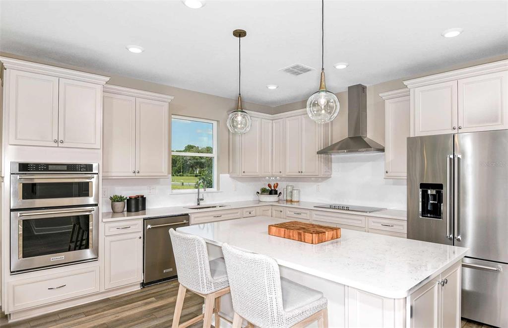 A modern kitchen features light-colored cabinetry, a large white island, and stainless steel appliances — 14822 SUNBEAM STREET, PARRISH, FL