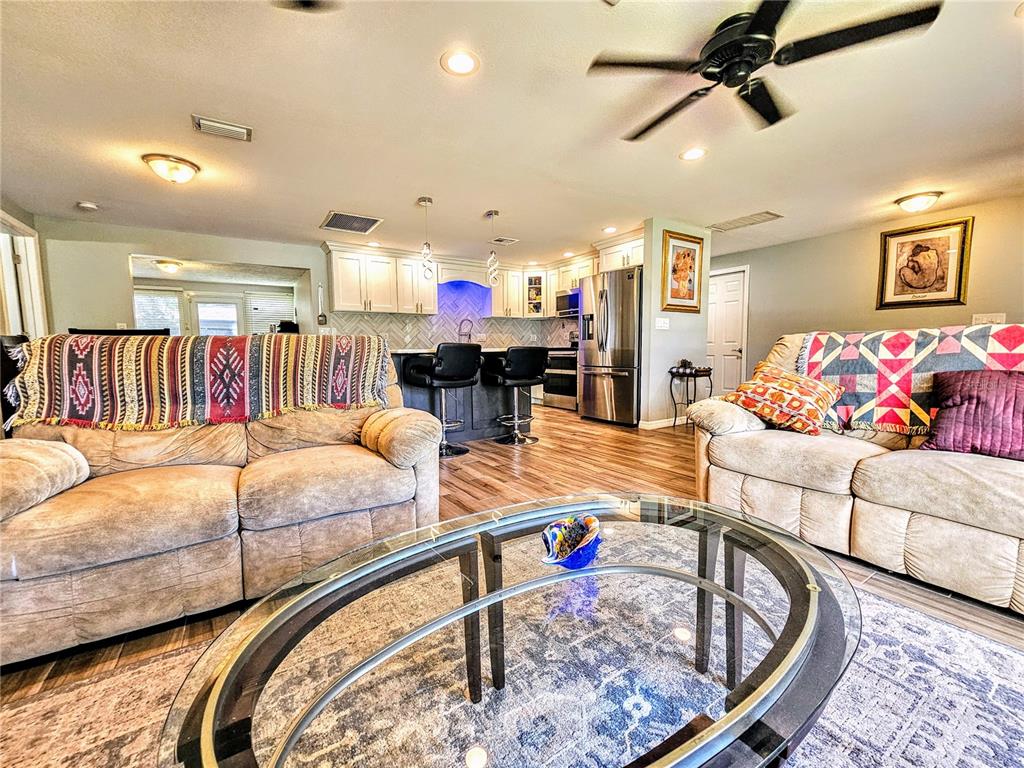 A living room with two sofas and a glass coffee table opens to a kitchen — 5650 BITTERSWEET DRIVE, HOLIDAY, FL