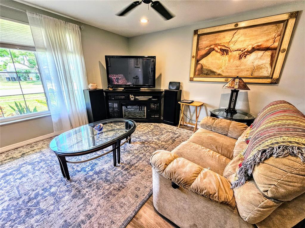 A living room features a tan sofa, a glass coffee table, and a large wall painting — 5650 BITTERSWEET DRIVE, HOLIDAY, FL