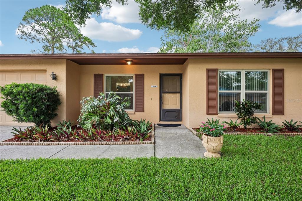 The exterior of a single-story house features tan stucco walls, brown shutters, and landscaping — 3718 SAND PEBBLE DRIVE, VALRICO, FL