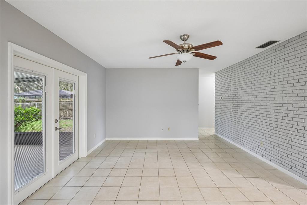 A room with light tile flooring, gray walls, a brick accent wall, and glass doors — 3718 SAND PEBBLE DRIVE, VALRICO, FL