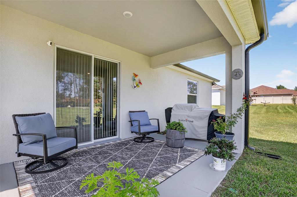 A covered patio features a patterned rug, two swivel chairs, and a covered Blackstone grill — 9839 SW 40TH TERRACE, OCALA, FL
