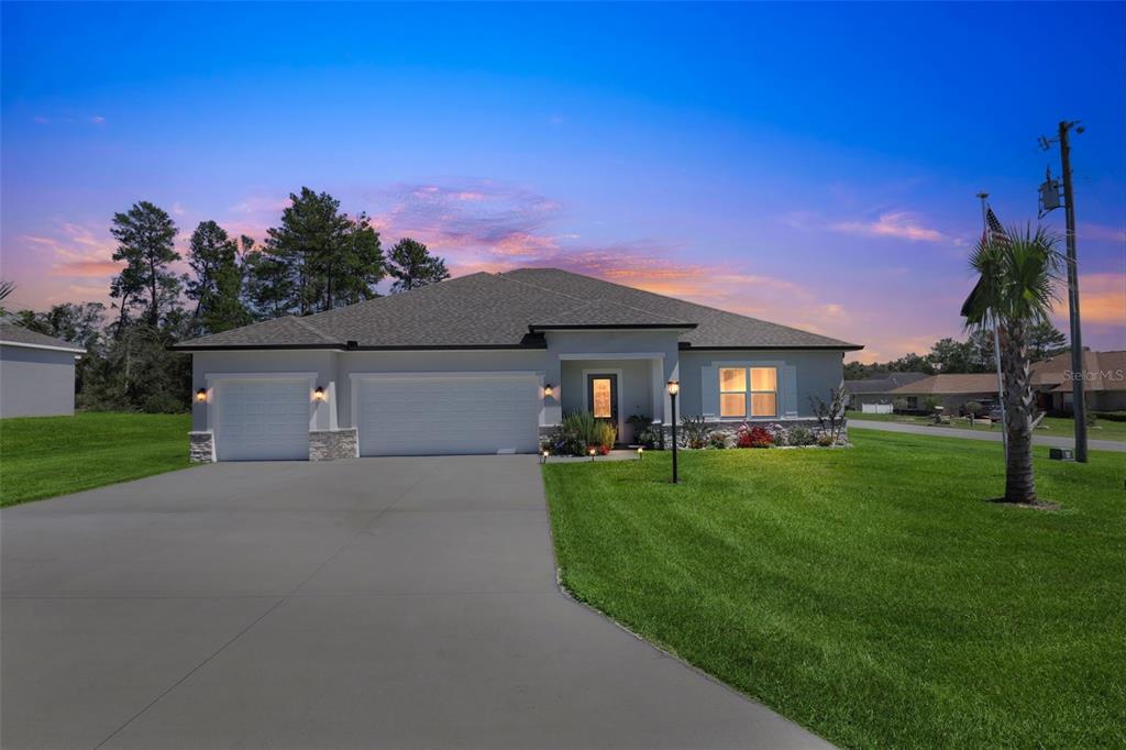 A single-story house with a three-car garage, stone accents, and a concrete driveway at dusk — 9839 SW 40TH TERRACE, OCALA, FL