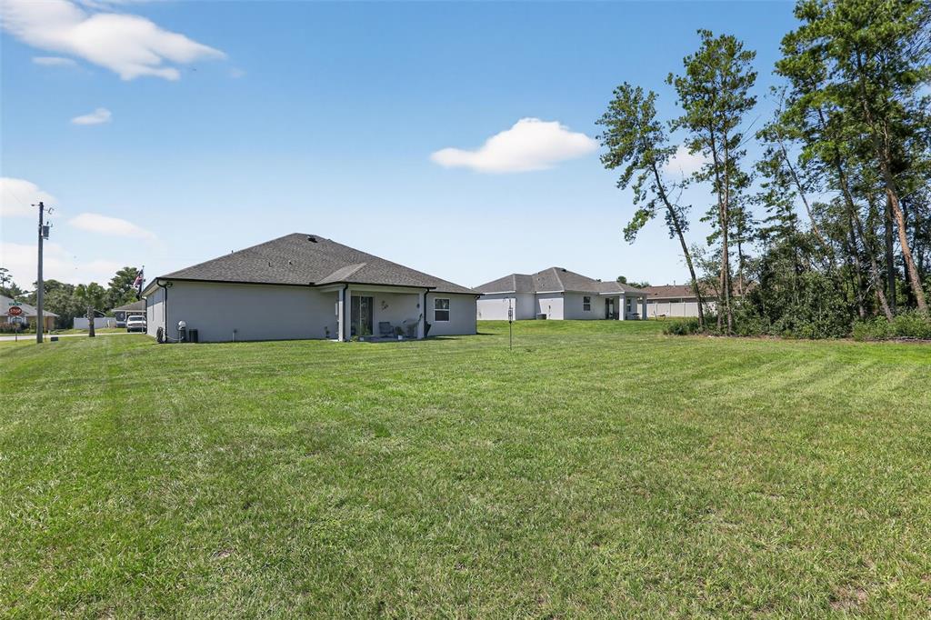 A view of the grassy backyard and rear exterior of a single-story suburban house — 9839 SW 40TH TERRACE, OCALA, FL