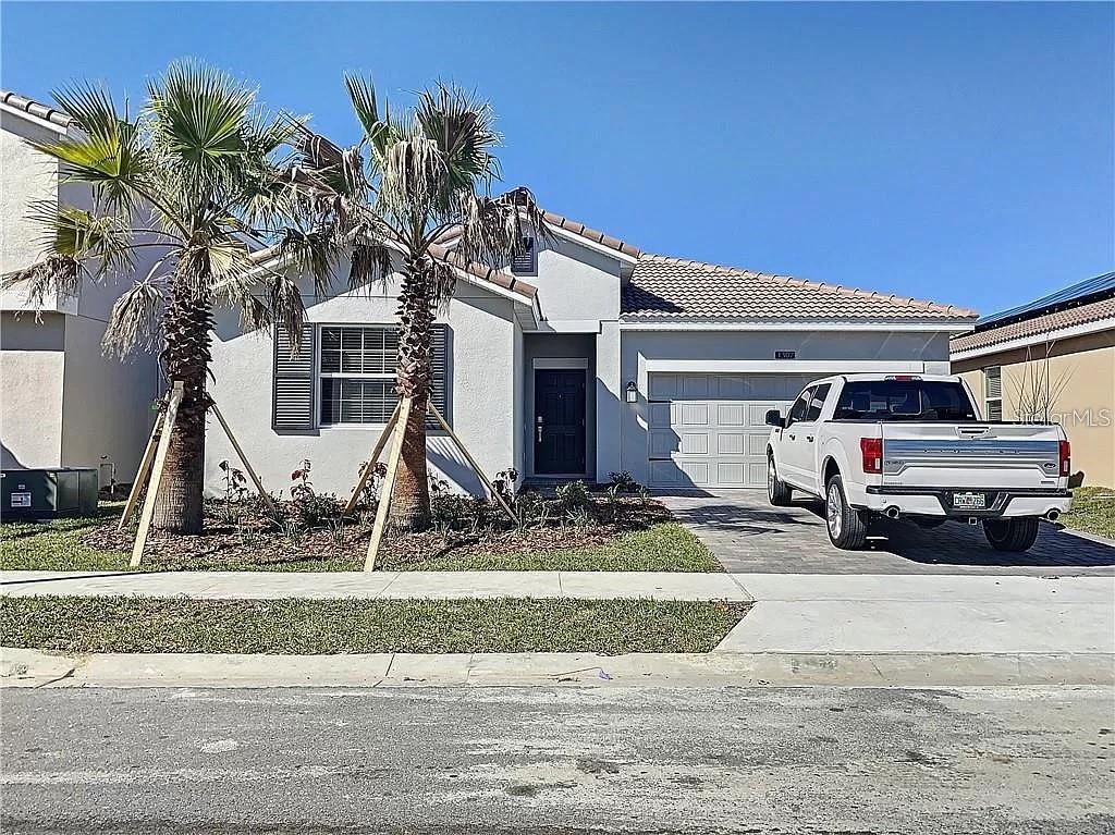 A single-story house with a white stucco exterior, a two-car garage, and two palm trees — 1307 OAK CREST STREET, DAVENPORT, FL