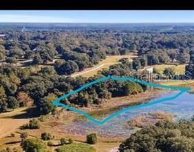 An aerial view shows a wooded plot of land outlined in blue next to a lake — 160TH, WEIRSDALE, FL