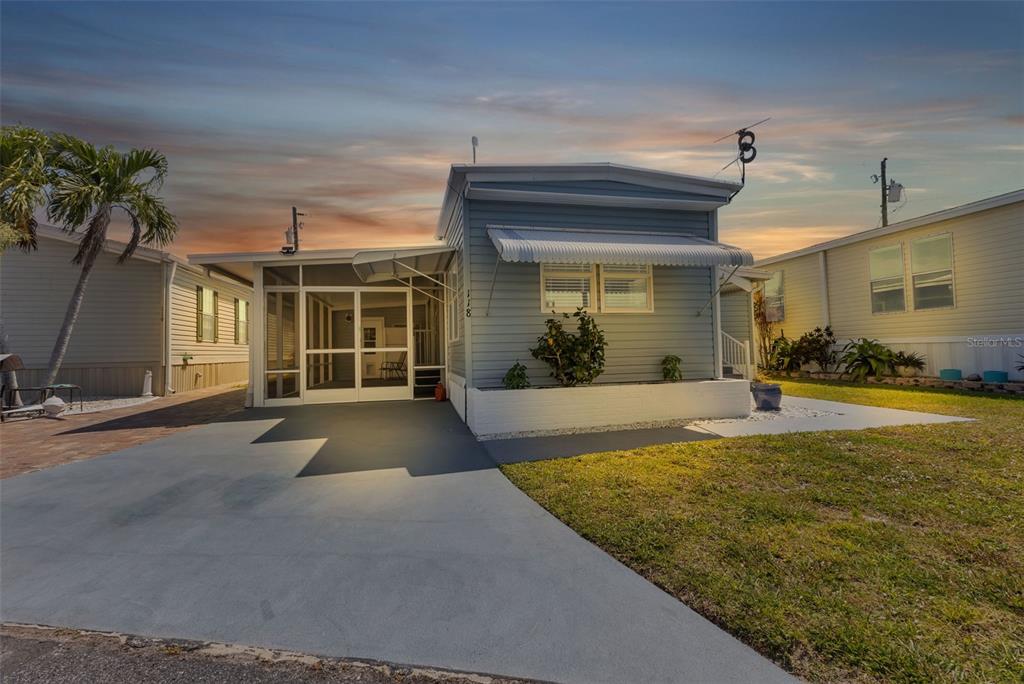A light blue mobile home with a screened-in porch and a concrete driveway at sunset — 10100 BURNT STORE ROAD UNIT 118, PUNTA GORDA, FL