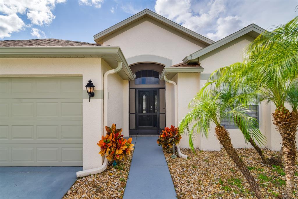 The exterior of a single-story home features a beige stucco facade, a garage, and a walkway — 20520 HOMOSSASA COURT, LAND O LAKES, FL
