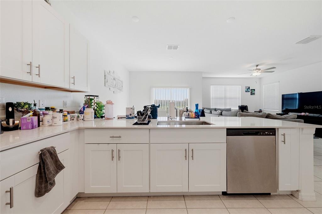 A kitchen with white cabinets, quartz countertops, and stainless steel appliances opens to a living area — 10336 LAVENDER ASTER TRAIL, SAN ANTONIO, FL