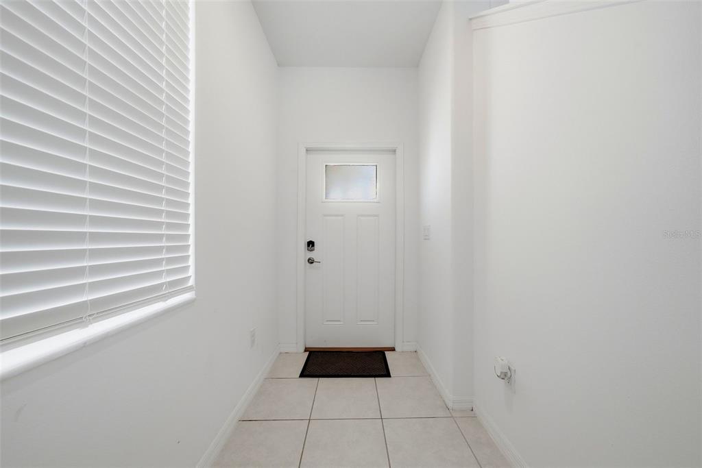 A narrow entryway features white walls, tiled flooring, a window with blinds, and a front door — 10336 LAVENDER ASTER TRAIL, SAN ANTONIO, FL