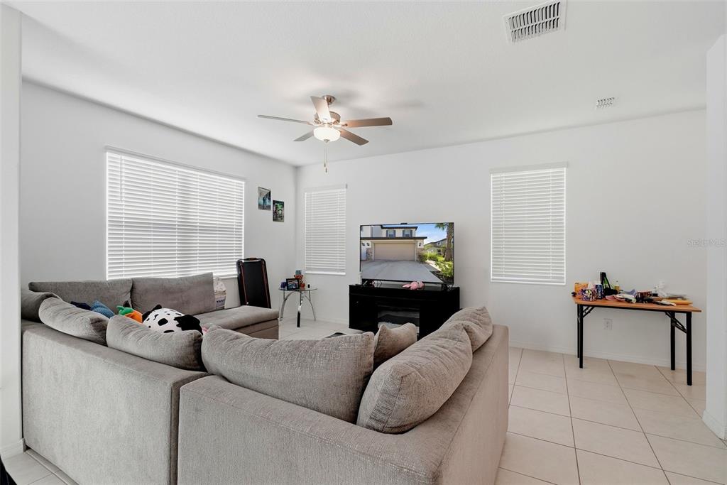 A living room features a grey sectional sofa, a television on a stand, and tile flooring — 10336 LAVENDER ASTER TRAIL, SAN ANTONIO, FL