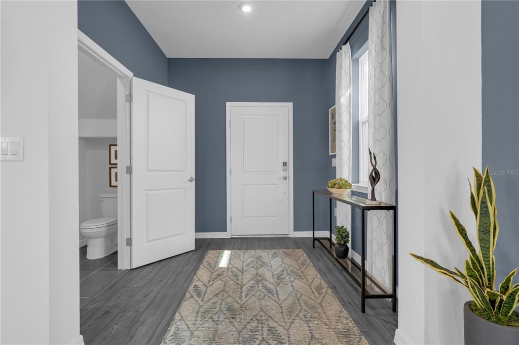 A foyer with blue walls, gray wood-look flooring, a console table, and an adjacent bathroom — 3812 SENNA WAY, TAVARES, FL