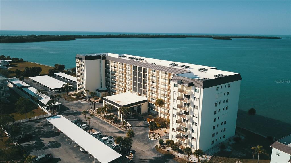 An aerial view of a multi-story apartment building with a parking lot near water — 9 HAIG PLACE UNIT 101, DUNEDIN, FL