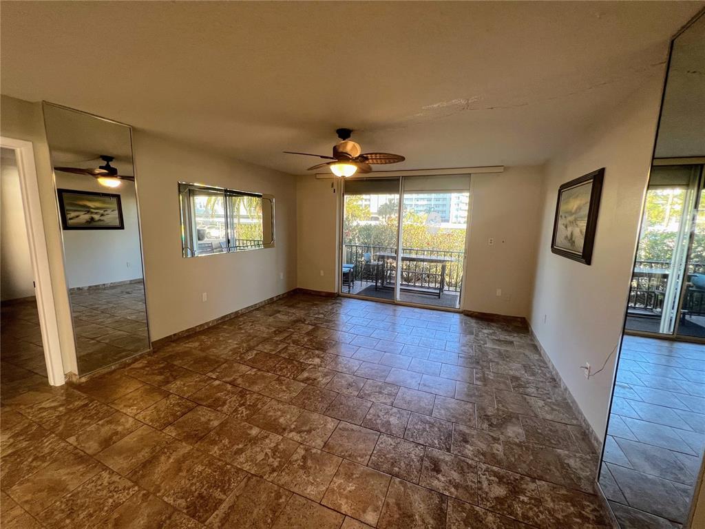 A living room features tile flooring, a ceiling fan, mirrored walls, and a sliding glass door — 9 HAIG PLACE UNIT 101, DUNEDIN, FL