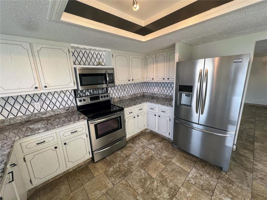 A kitchen features white cabinets, stainless steel appliances, granite countertops, and a tiled backsplash — 9 HAIG PLACE UNIT 101, DUNEDIN, FL