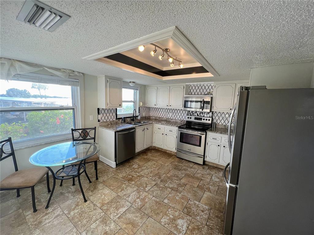 A kitchen features white cabinets, stainless steel appliances, patterned tile backsplash, and a glass table — 9 HAIG PLACE UNIT 101, DUNEDIN, FL