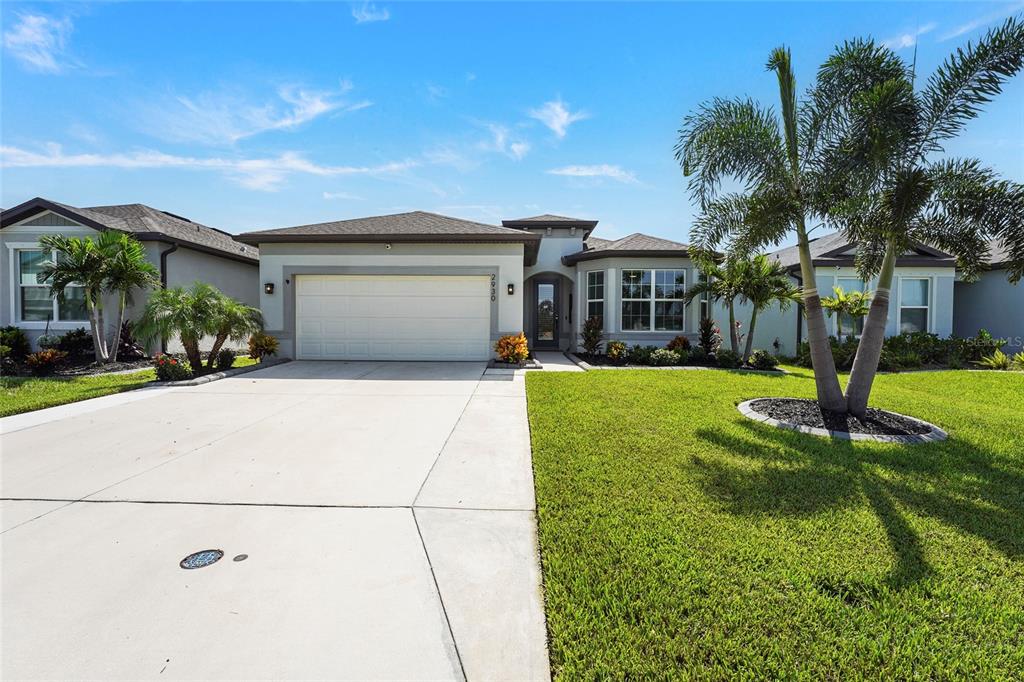 A single-story suburban house with a two-car garage, manicured lawn, and palm trees — 2930 61ST DRIVE E, ELLENTON, FL