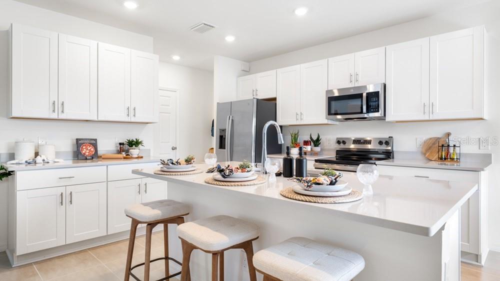 A modern kitchen features white cabinetry, stainless steel appliances, and a large quartz-topped island — 12206 WISPY CLOUD WAY, HUDSON, FL