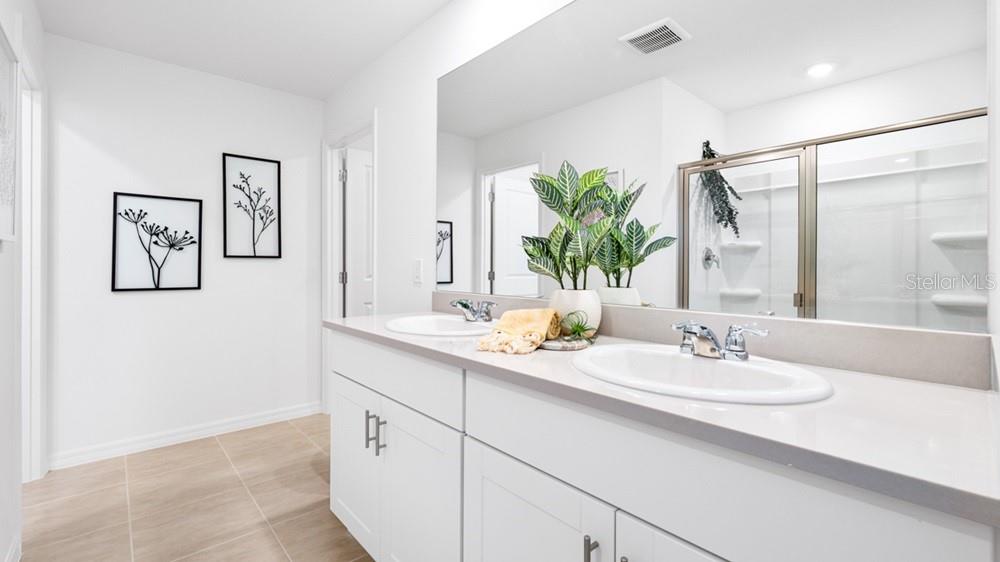 A bathroom features a double vanity with white cabinets, a large mirror, and a shower — 12206 WISPY CLOUD WAY, HUDSON, FL