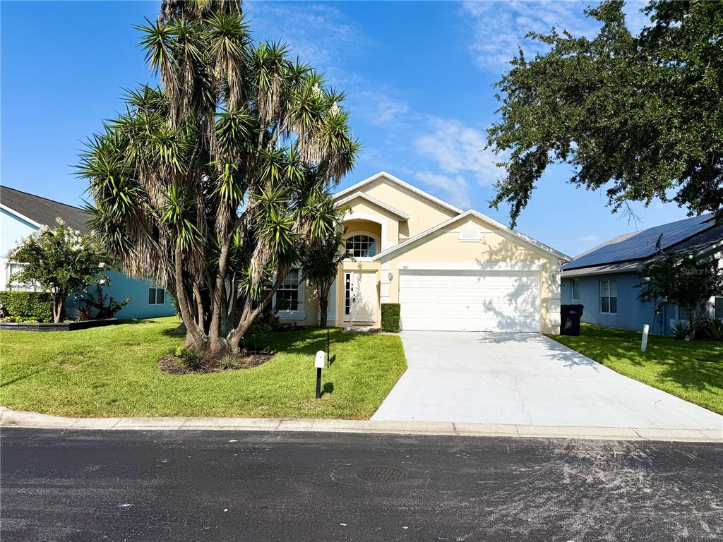 A two-story suburban house with a concrete driveway, a large palm tree, and a garage — 207 LANGHAM DRIVE, DAVENPORT, FL