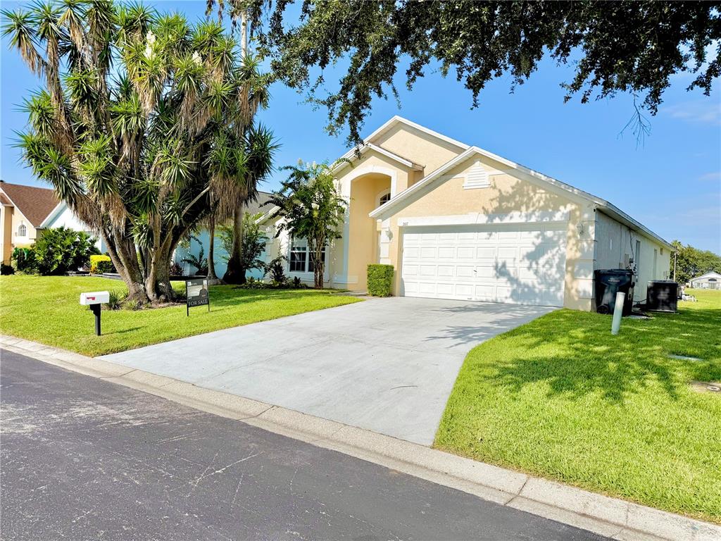 A single-story suburban house with a beige stucco exterior, a two-car garage, and a driveway — 207 LANGHAM DRIVE, DAVENPORT, FL