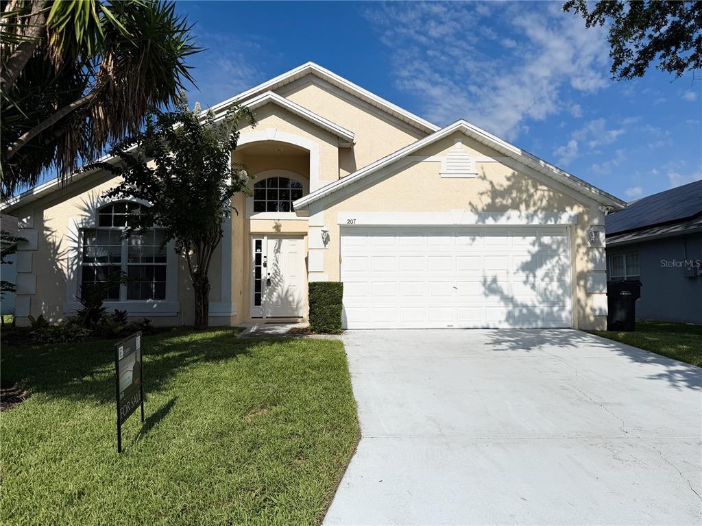 A single-story suburban house with a two-car garage, beige stucco siding, and a concrete driveway — 207 LANGHAM DRIVE, DAVENPORT, FL
