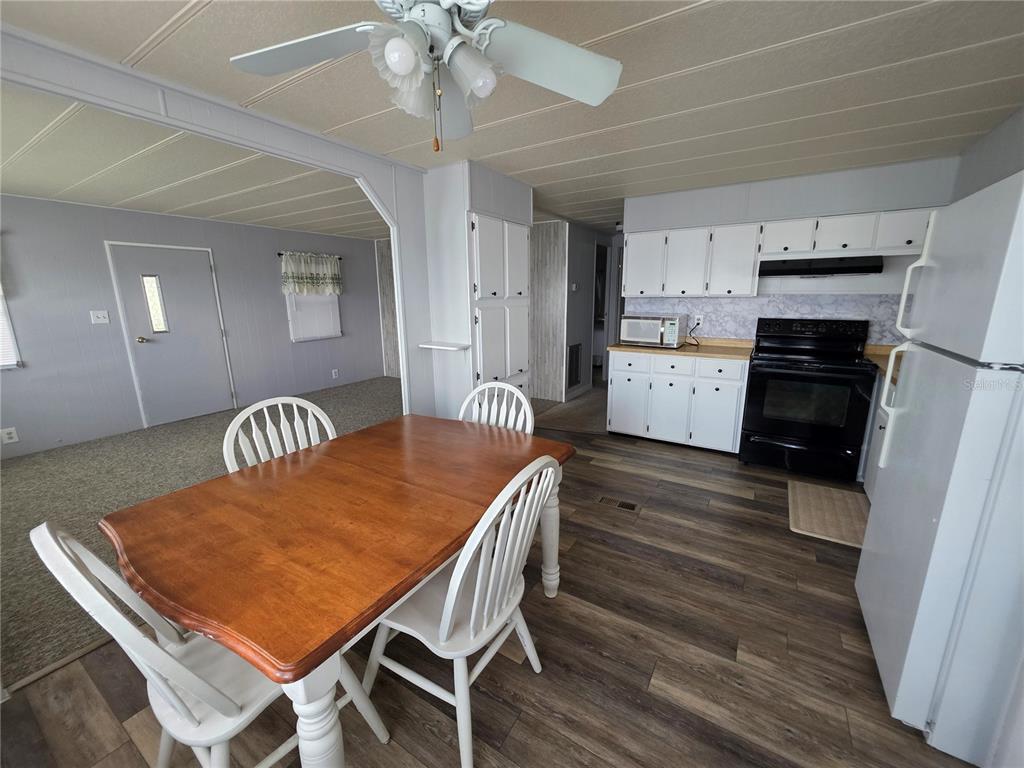 A dining area with a wooden table and chairs sits adjacent to a white kitchen — 4603 NEWCOMB AVENUE, ZEPHYRHILLS, FL