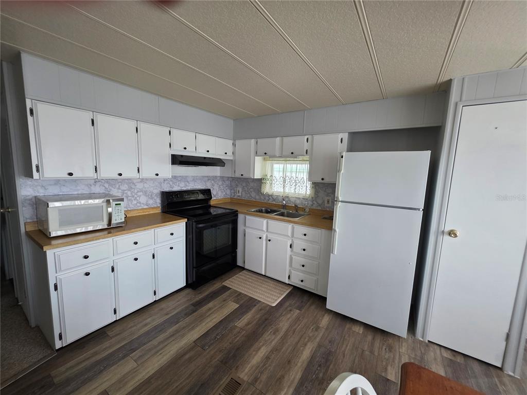 A kitchen features white cabinets, a black stove, a microwave, and a white refrigerator — 4603 NEWCOMB AVENUE, ZEPHYRHILLS, FL
