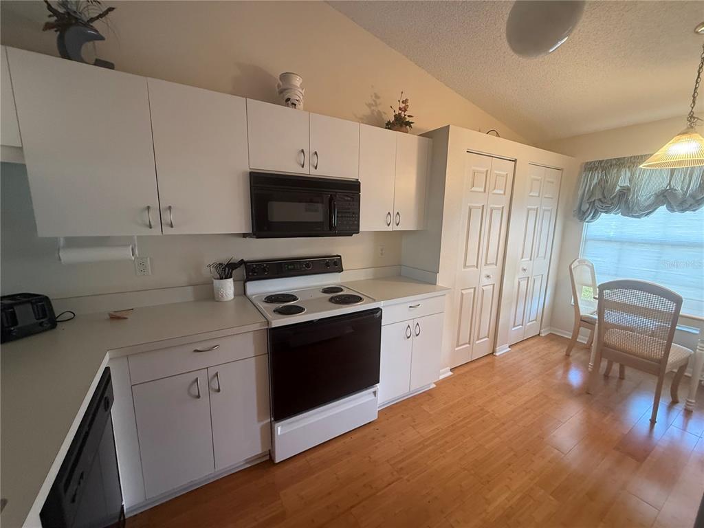 A kitchen features white cabinetry, a black microwave and stove, and light wood flooring — 4211 CADDIE DRIVE E UNIT 202, BRADENTON, FL