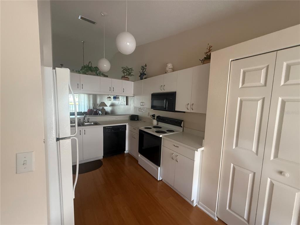 A kitchen features white cabinets, black appliances, wood flooring, and two pendant lights — 4211 CADDIE DRIVE E UNIT 202, BRADENTON, FL