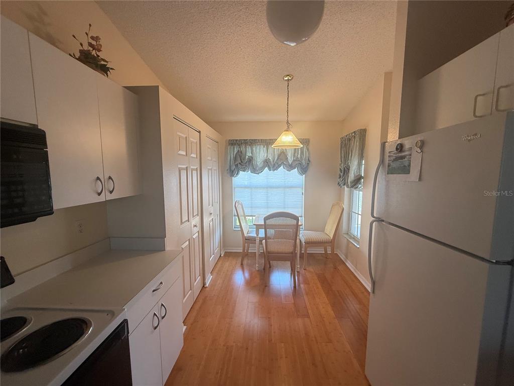 A kitchen with white cabinets, a white refrigerator, and a small dining area with wood flooring — 4211 CADDIE DRIVE E UNIT 202, BRADENTON, FL