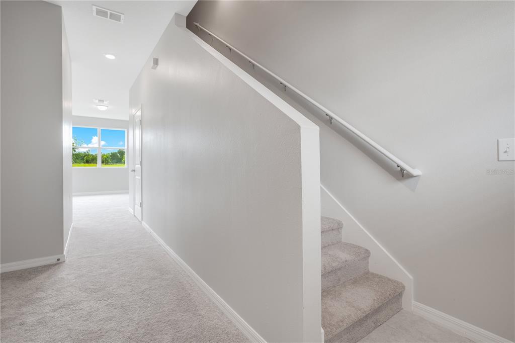 A carpeted hallway leads to a windowed room beside a staircase with a white railing — 1068 APPLETON STREET, DAVENPORT, FL