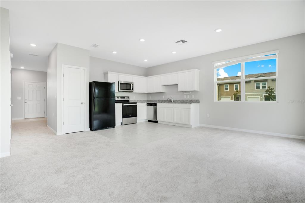 A kitchen with white cabinets, stainless steel appliances, and a black refrigerator, adjacent to carpeted space — 1068 APPLETON STREET, DAVENPORT, FL
