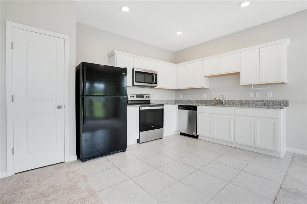 A kitchen features white cabinets, granite countertops, tile flooring, and a mix of black appliances — 1068 APPLETON STREET, DAVENPORT, FL