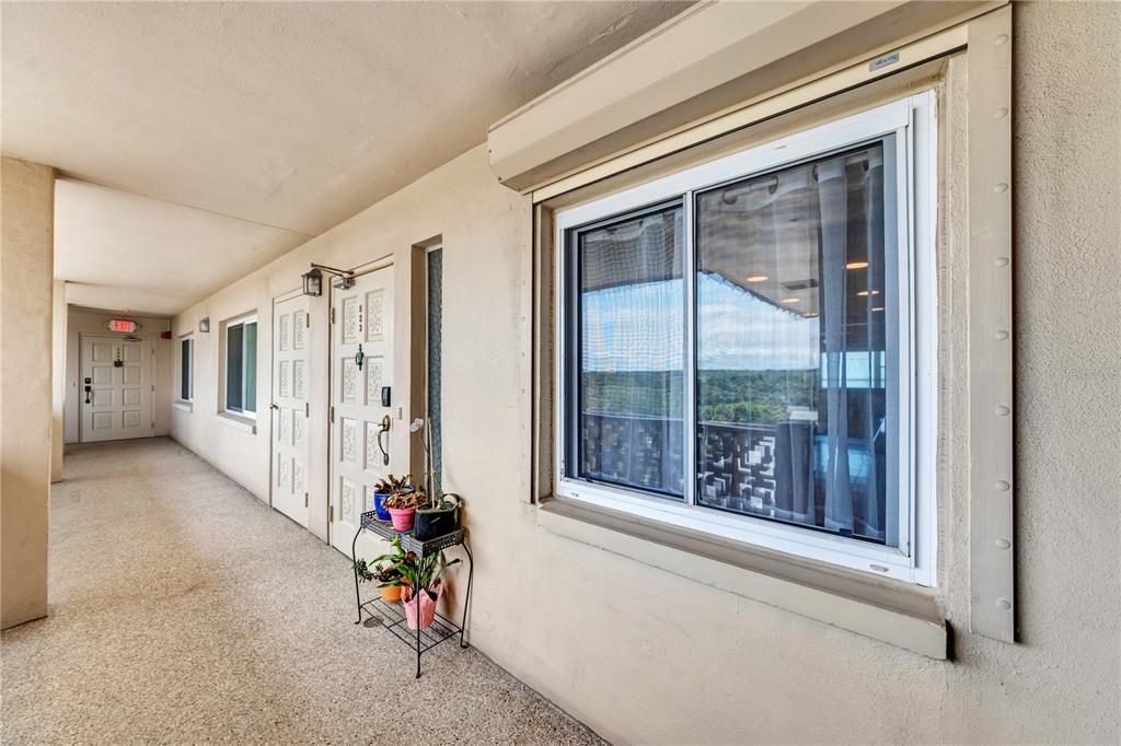 An outdoor apartment hallway features a beige stucco wall, a sliding window, and unit doors — 622 EDGEWATER DRIVE UNIT 823, DUNEDIN, FL