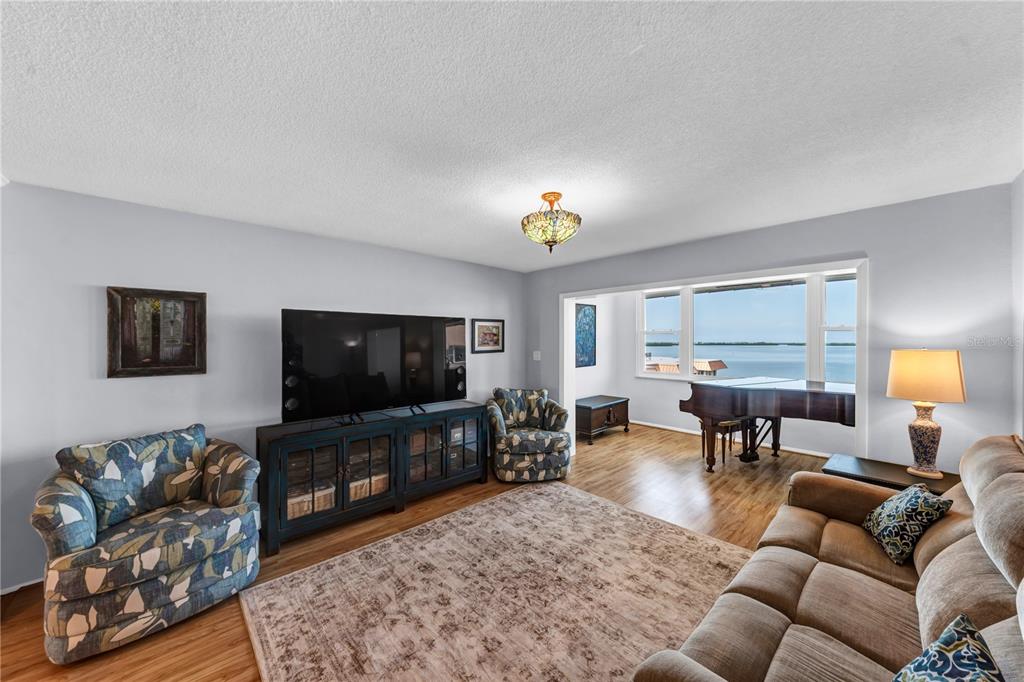 A living room features a large television, patterned armchairs, a sofa, and a grand piano — 622 EDGEWATER DRIVE UNIT 823, DUNEDIN, FL