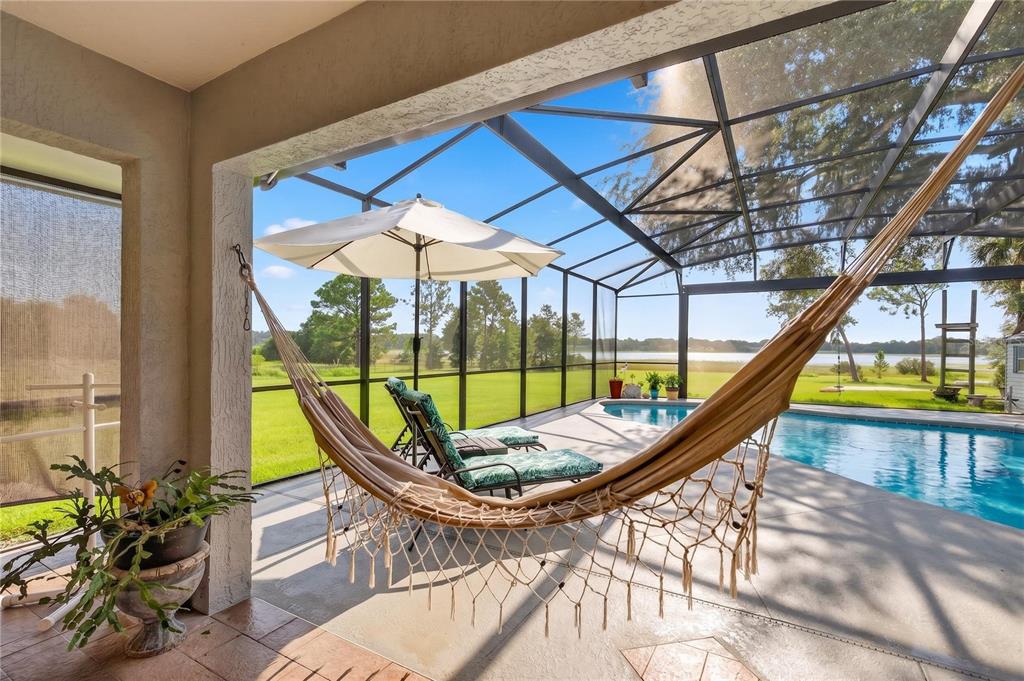A screened-in patio features a hammock, lounge chairs, a pool, and a view of water — 19923 W ELDORADO DRIVE, EUSTIS, FL