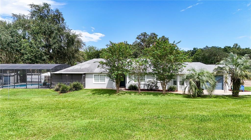 A single-story house with a screened pool enclosure and a large green lawn — 19923 W ELDORADO DRIVE, EUSTIS, FL