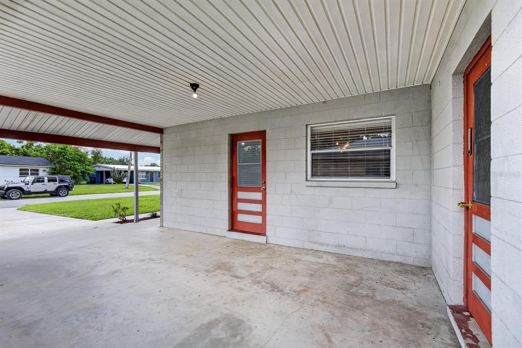 A concrete carport features a white ceiling, two red doors, and a single window — 403 ALMA DRIVE, BRANDON, FL