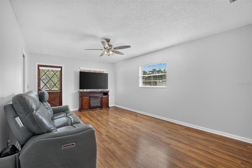 A living room features gray walls, wood-look flooring, a ceiling fan, and a gray reclining sofa — 403 ALMA DRIVE, BRANDON, FL