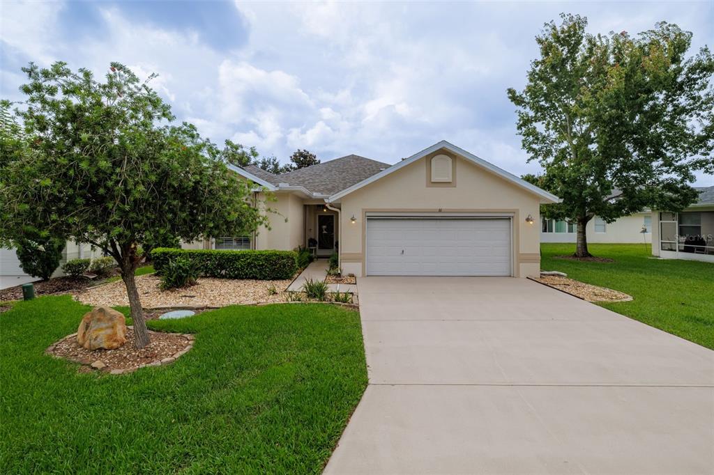 A single-story house with a beige exterior, a white garage door, and a landscaped front yard — 61 RAINTREE CIRCLE, PALM COAST, FL