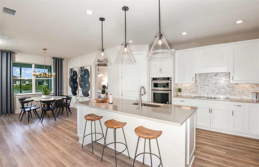 A modern kitchen features a large island with bar stools, white cabinetry, and pendant lighting — 14745 SUNSET CREST LANE, PARRISH, FL