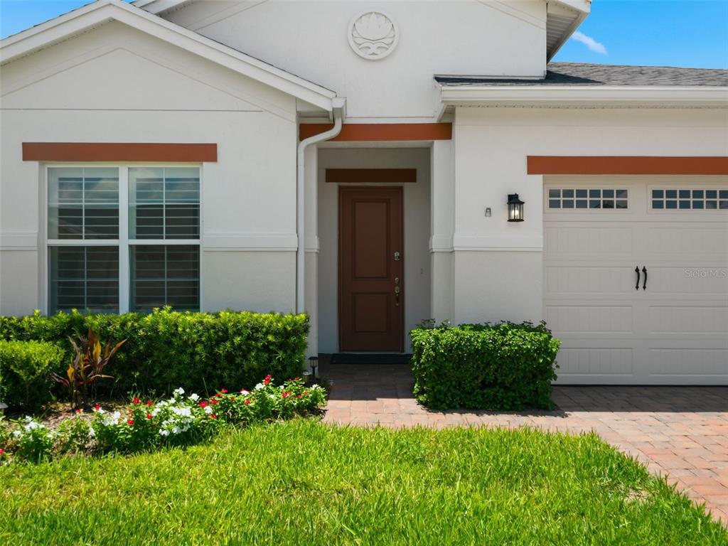 The exterior of a house features a brown front door, a garage, and landscaped bushes — 2680 REDBLUSH TERRACE, ST CLOUD, FL