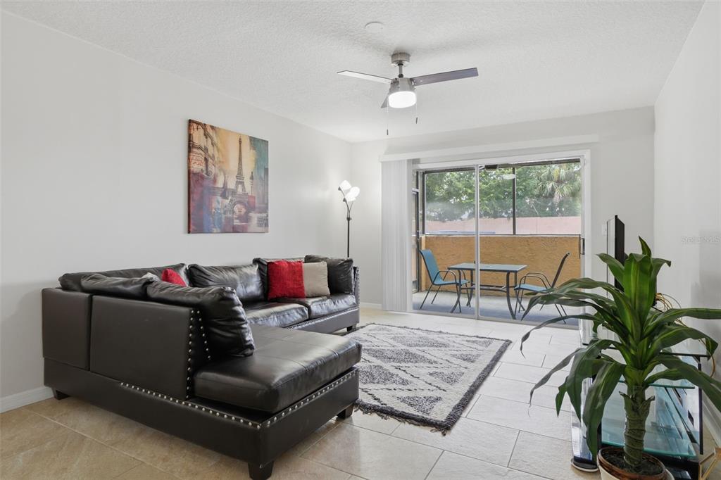 A living room features a black sectional sofa, tile flooring, and a sliding glass door — 648 KENWICK CIRCLE UNIT 102, CASSELBERRY, FL