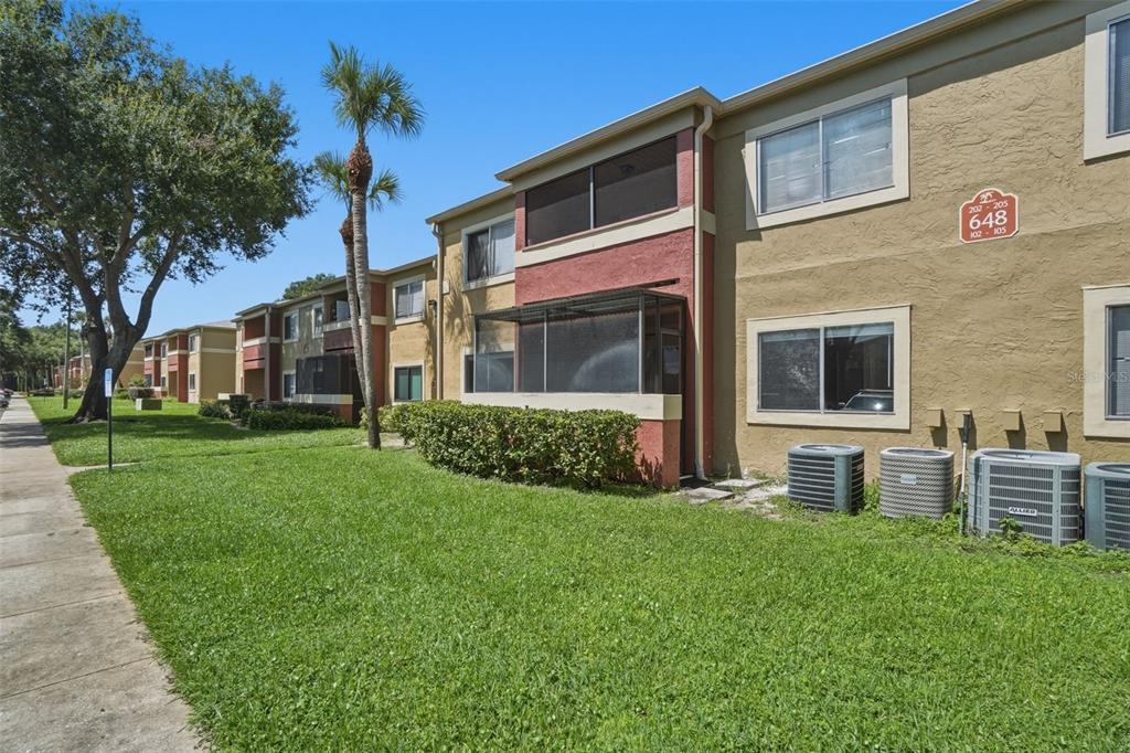 A multi-story apartment building exterior with tan and red stucco walls and screened-in balconies — 648 KENWICK CIRCLE UNIT 102, CASSELBERRY, FL
