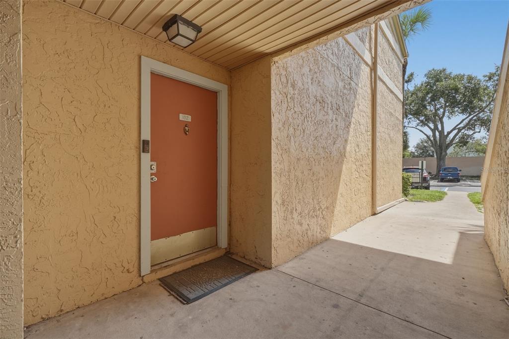 An exterior view of a residential unit entrance with an orange door and concrete walkway — 648 KENWICK CIRCLE UNIT 102, CASSELBERRY, FL